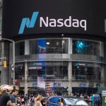 Traders monitor Nasdaq index on multiple screens with green bullish charts rising sharply amid red warning signals flashing in the background