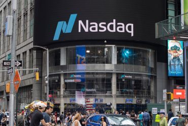Traders monitor Nasdaq index on multiple screens with green bullish charts rising sharply amid red warning signals flashing in the background