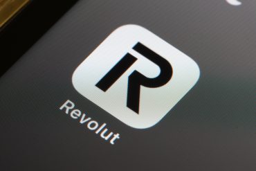 Revolut app interface on smartphone, with digital finance icons, charts, and a rising valuation arrow, symbolizing fintech expansion and revenue growth.