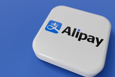 Customer tapping phone at checkout terminal with Alipay logo visible, showcasing contactless NFC payment in a Chinese retail store.