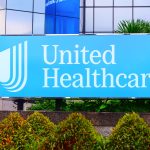UnitedHealth headquarters with falling stock chart and rising healthcare cost visuals symbolizing forecast downgrade and industry pressure.