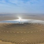 Aerial view of a solar power plant with circular arrangement of mirrors in a desert landscape under clear blue skies.