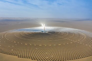 Aerial view of a solar power plant with circular arrangement of mirrors in a desert landscape under clear blue skies.
