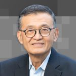 Intel CEO Lip-Bu Tan speaking at tech conference with U.S. and China flags blurred in background, symbolizing geopolitical tension and corporate scrutiny