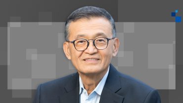 Intel CEO Lip-Bu Tan speaking at tech conference with U.S. and China flags blurred in background, symbolizing geopolitical tension and corporate scrutiny