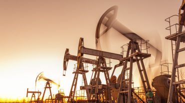 Oil refinery towers and drilling pumps at sunset representing peak U.S. energy production