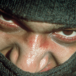 Close-up of a masked figure in a black balaclava with a hostile gaze.