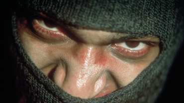 Close-up of a masked figure in a black balaclava with a hostile gaze.