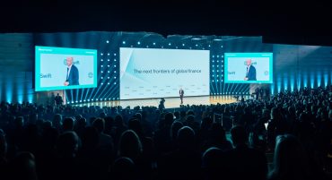 Conference stage at Sibos 2025 with SWIFT executives announcing blockchain initiative