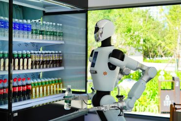 Galbot humanoid robot salesperson delivers a drink for a customer at the 9-square-meter bus shop in ART PARK on August 10, 2025 in Beijing, China. Galbot, the developer of the robot, plans to establish 100 stores across 10 cities in China this year, with expectations of serving up to 2,000 customers per store every day. (Photo by Song Jiaru/VCG via Getty Images)