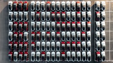 Aerial view of rows of new cars parked at an automotive plant, symbolizing production scale and consumer demand in the auto industry.