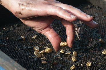Gold panning with sieve and raw nuggets illustrating physical gold sourcing amid rising global prices