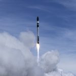 Electron rocket ascends during launch, leaving a bright exhaust plume against a clear sky as vertical integration becomes the key competitive edge in a consolidating space economy.