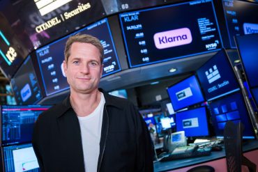 Klarna CEO, Sebastian Siemiatkowski on New York Stock Exchange trading floor with Klarna branding on screens.