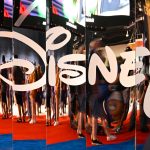 Disney+ logo photographed in the mirror, as Disney invests $1B in OpenAI, licensing 200+ characters for Sora and adopting ChatGPT enterprise tools, testing whether generative AI can reshape entertainment.