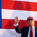 President Donald Trump stands before an American flag as the White House moves to halt a planned AI oversight order and prioritize U.S. leadership in artificial intelligence.