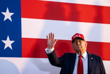 President Donald Trump stands before an American flag as the White House moves to halt a planned AI oversight order and prioritize U.S. leadership in artificial intelligence.